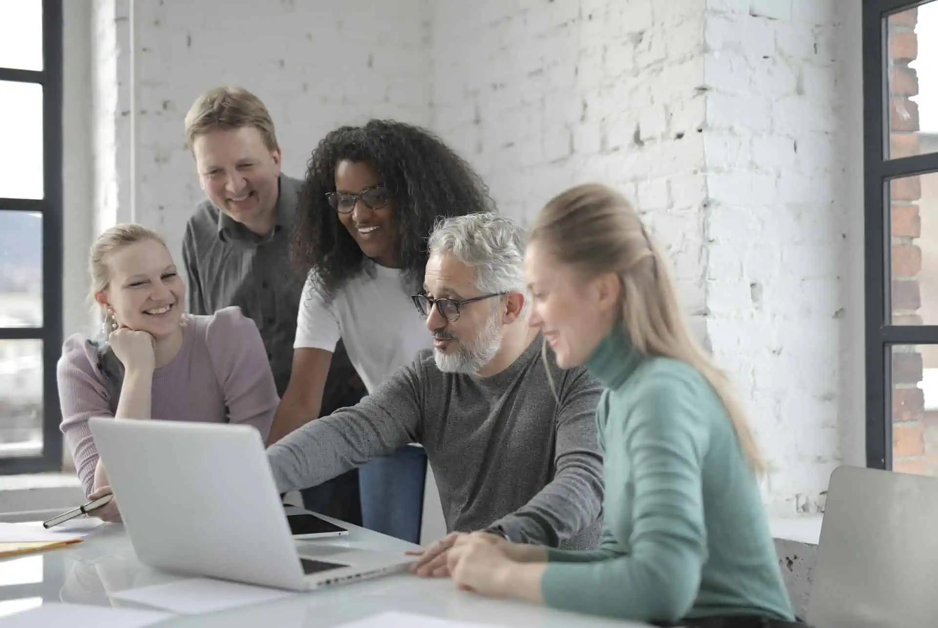 Group of coworkers smiling while reviewing laptop together